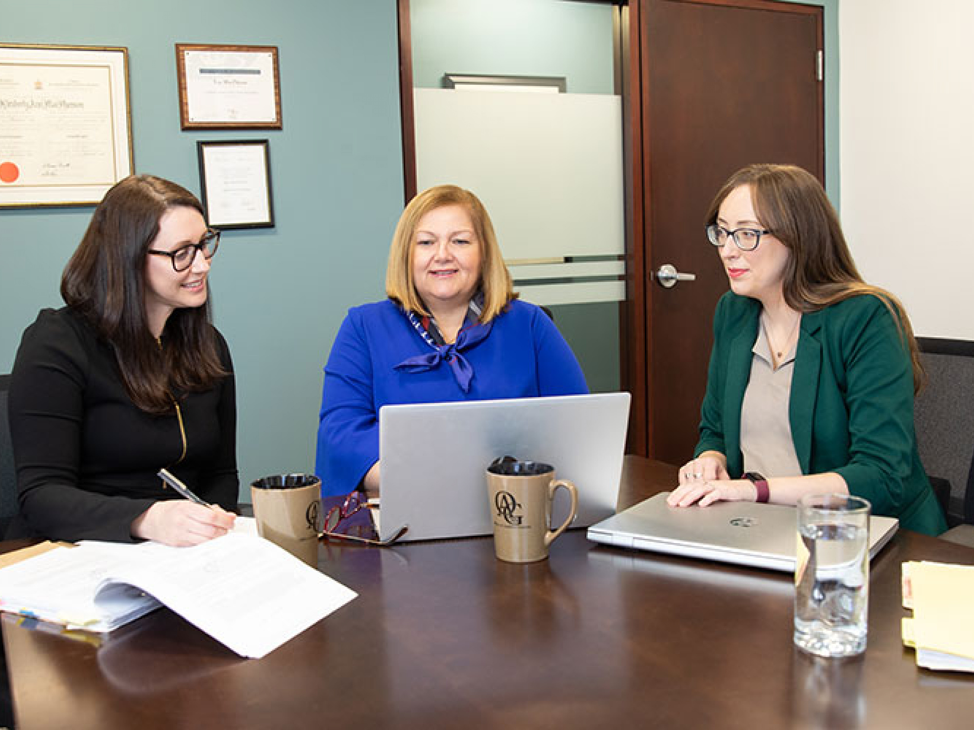 Three women in office reviewing resumes on laptop.